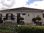 Free-standing single storey vernacular cottage; full hipped corrugated iron roof behind a parapet wall; sash windows with leaded lights; modern stock stable door; stoep enclosed creating two projecting wings and a recessed entrance doorway; low plastered Type of site: House Current use: House.