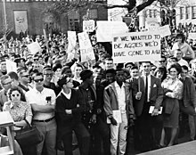 A crowd of students tightly packed together during a protest, many with signs, one in the foreground that reads "If we had wanted to be Aggies we'd have gone to A&M"