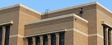 Photograph showing crisply horizontal rooflines of three bays of the courthouse at various heights and brickwork below. Terra cotta capitals atop vertical pilasters show in in two of the bays, illustrating the rectilinear Prairie School style with its emphasis on horizontal lines accented by contrasting vertical lines.