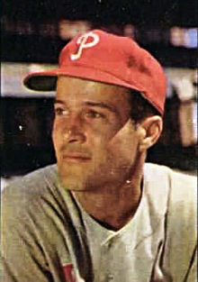 A smiling man wearing a red baseball cap with a white "P" on the face and looking to the left of the image