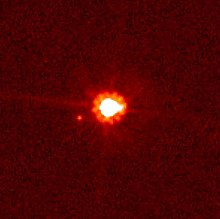 Image rougeâtre où un gros point blanc central au halo rouge est accompagné d'un autre plus petit.