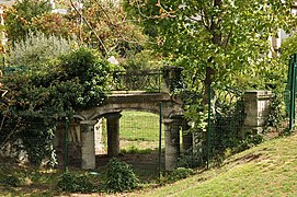 Pont en pierre de taille à trois arcs surbaissés qui enjambe un fossé aujourd’hui asséché, partiellement ombragé. Le grand arc central repose sur quatre colonnes rondes, deux de chaque côté. Deux arcs plus petits vont jusqu’aux culées. Ces dernières supportent les escaliers montant sur le pont. Garde-corps métalliques. La végétation envahit progressivement le pont de chaque côté.