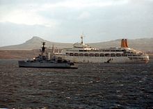 A grey warship passes by a white cruise ship with prominent red funnels