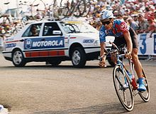 A man wearing a cycling uniform while riding a bike and preparing to turn.