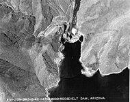 The downstream face of renovated Roosevelt Dam, with a concrete face. A bridge spanning Lake Roosevelt is seen in the background.