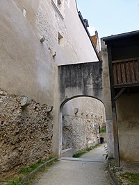 Photographie en couleurs d'un chemin bitumé longeant des structures urbaines et passant sous une arcade.