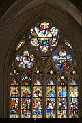 Vue en contre-plongée du vitrail de la Vierge avec six parties en hauteur avec de nombreux personnages et trois rosaces au-dessus