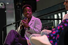 Emma Obanye speaking into a microphone while looking at the person sitting next to her.