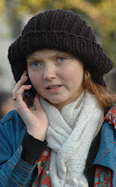 the head and shoulders of Cole outside on a mobile phone wearing a black beret, blue coat and white scarf