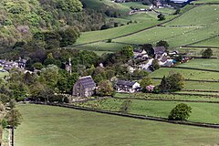 Green fields with walls, and a small village on the left with a tall chapel and water tower prominent on the skyline