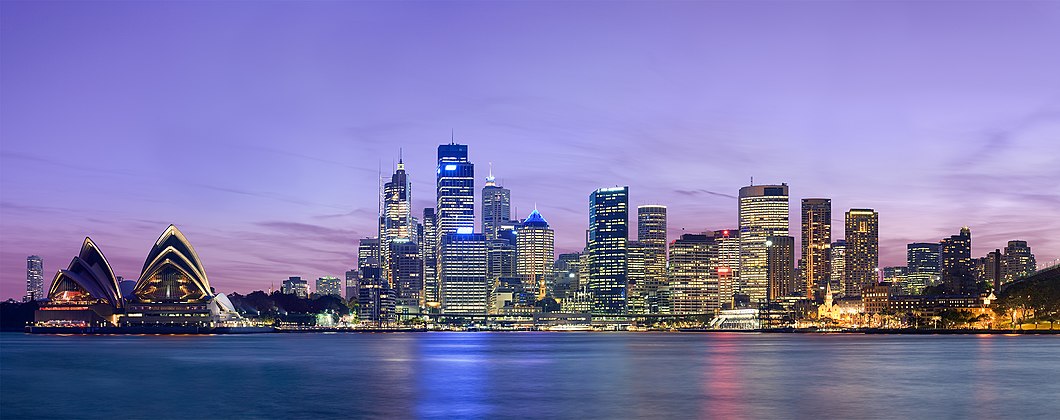 Panorama Sydney za soumraku, metropole svazového státu Nový Jižní Wales, kterou v roce 1788 založil admirál Arthur Phillip jako britskou vězeňskou kolonii okolo zálivu Port Jackson. S populací 4,9 milionů obyvatel Sydney představuje nejlidnatější město v Austrálii. Vlevo stojí operní dům navržený dánským architektem Jørnem Utzonem a napravo se tyčí mrakodrapy centrální obchodní oblasti.