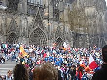 A view of the celebratory vibe outside the Cologne Cathedral in Germany (2005). The participation of Catholics from many countries worldwide results in an enhanced and collaborate spiritual experience. Cologne 2005 WYD.jpg