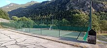 Photographie d'un court de tennis vert en contrebas de la montagne et protégé par des grillages verts.