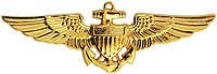 A golden badge depicting a shield superimposed over an anchor and a pair of wings