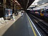 A platform with several people waiting for a train. A white square sign has a London Underground roundel with 