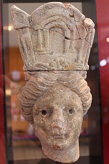 Photographie de la tête d'une statue féminine portant une coiffure allégorique.