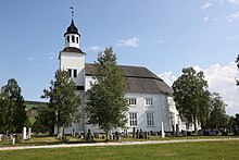 Foto einer weißen Holzkirche, im Vordergrund ein Friedhof