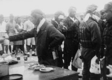 Photo noir et blanc d'un groupe de pilotes en tenue de vol. L'un d'entre eux tend la main droite vers un objet hors cadre.