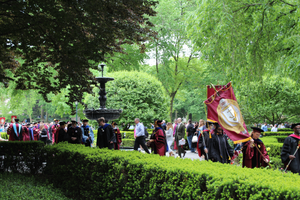 Students and faculty in commencement garb walking down pathway among greenery