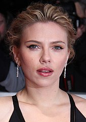 An image of Scarlett Johansson posing for the camera with paparazzi in the background.