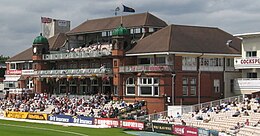 An ornate brick building with two towers, with stands in front.