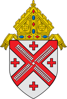 Shield topped by a mitre, featuring a silver field divided per red saltire, four red crosses within the four quarters, and a silver wind mill on the saltire
