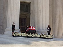 Ginsburg's casket at the top of the Supreme Court steps, flanked by two of her former law clerks and an honor guard from the Supreme Court Police Ruth Bader Ginsburg lying in repose at the top of the steps to the United States Supreme Court.jpg