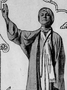 A white woman wearing a turban and robes, one arm raised in a gesture of command or benediction.