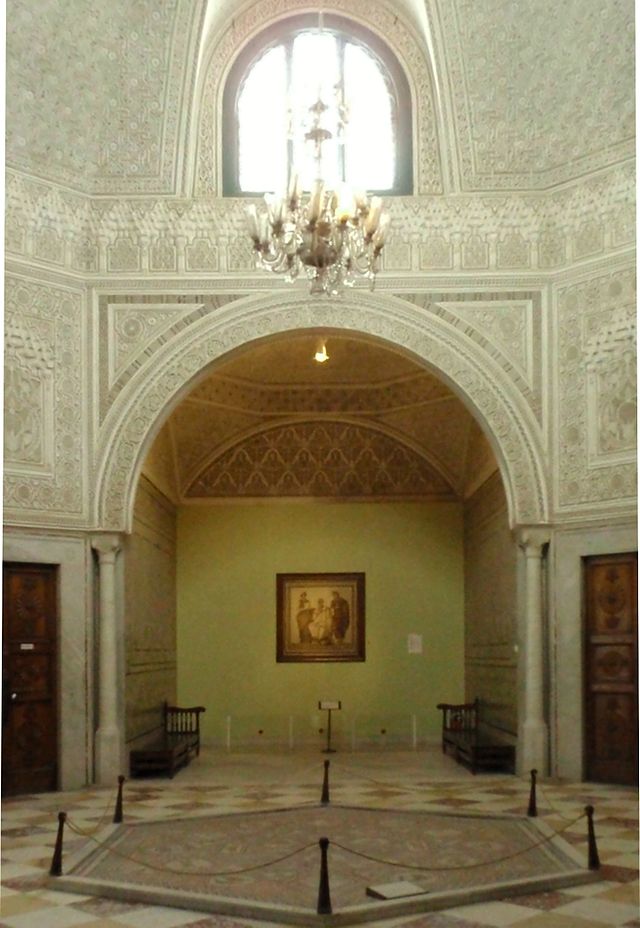 Photographie de la salle de Virgile montrant la mosaïque de Virgile et le plafond de stuc richement sculpté du palais.