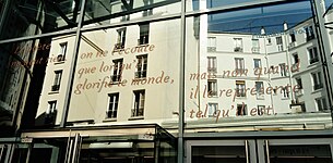 Sur une façade de verre est écrit en italiques dans une couleur orangée : « Le poète ne peut rien, on ne l'écoute que lorsqu'il glorifie le monde, mais non quand il le représente tel qu'il est.»