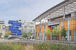 A large building faced with panels of wood and glass, and an arched roof, labelled "Confluence", is on the right. Other modern city buildings are across a bridge, on the left of the frame.