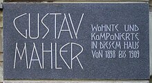  A dark plaque with white lettering in which the composer's name is shown in extra large characters on the left, the main message in smaller characters on the right