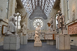 Photographie montrant plusieurs sculptures et statues dans une ancienne église ; toiture en verre et rosace.