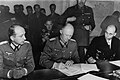 Alfred Jodl, tussen Major Wilhelm Oxenius (links) en Generaladmiral Hans-Georg von Friedeburg (rechts) ondertekenen de Duitse Overgave te Reims, Frankrijk, 7 mei 1945.