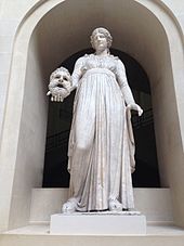 Statue d'une femme habillée d'une robe tenant un masque dans sa main droite.