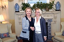 Photographie de deux femmes caucasiennes blondes dans un bureau en train de se serrer la main.