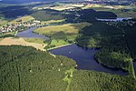 Вид с воздуха, показывающий несколько озер на плотине в лесном и городском ландшафте.