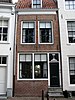 Huis met gepleisterde lijstgevel. Nok evenwijdig aan straat. Dakkapel