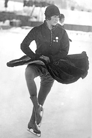 A female figure skater wearing a dark-colored dress and cloche hat performs a turn in an outdoor ice rink.