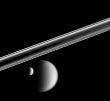 Photo noir et blanc. Les anneaux sont visibles au centre de l'image au-dessus de Titan et Rhéa, les autres lunes étant des points blancs.