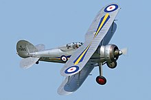 a colour photograph of a silver painted bi-plane fighter aircraft in flight