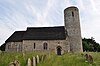 A stone church with thatched roofs seen from the north; on the left is a chancel with an apse, in the middle is the nave containing a Norman doorway, and on the right is a round tower