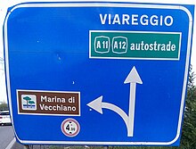 Example of directional road sign with multiple destinations. It is blue because it is on a main road (not a motorway) outside a town. The indication to a motorway is in a green box, and the indication to a geographical feature or a tourist attraction is in a brown box. It uses both allowed fonts: the words VIAREGGIO and Marina di Vecchiano are in Alfabeto Normale, and the word autostrade is in Alfabeto Stretto Italian road sign with mixed fonts.jpg