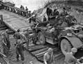 T-17E1 Staghound armoured car of the 12th Manitoba Dragoons crossing a Bailey bridge, Elbeuf, France, 28 August 1944. Soldiers are offloading railway ties to reinforce or smooth out the road surface.