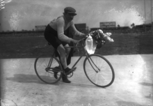 Photographie en noir et blanc d'un cycliste tenant un bouquet de fleurs dans les mains.