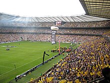 Vue d'un stade depuis une tribune : le terrain à gauche et une tribune remplie de supporters en jaune et noir à droite