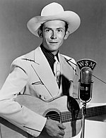 A black-and-white photo of Hank Williams holding a guitar.