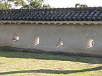 Photo of defensive loopholes in one of the castle walls. Two of the loopholes are rectangle-shaped, one is triangle-shaped, and one is circle-shaped.