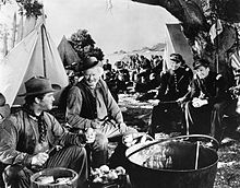 a gathering of men in an American West scene with the two in the foreground peeling potatoes