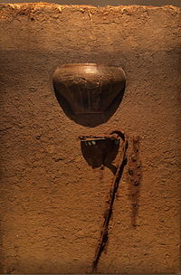 A reconstruction of Hamburg-Marmstorf grave 216. A shield, lance, and a slashing sword were found buried underneath a ceramic urn containing the ashes. The lance shaft probably stuck out of the ground to mark the grave. Urnenbestattung HH-Marmstorf Grab 216 Modell.jpg